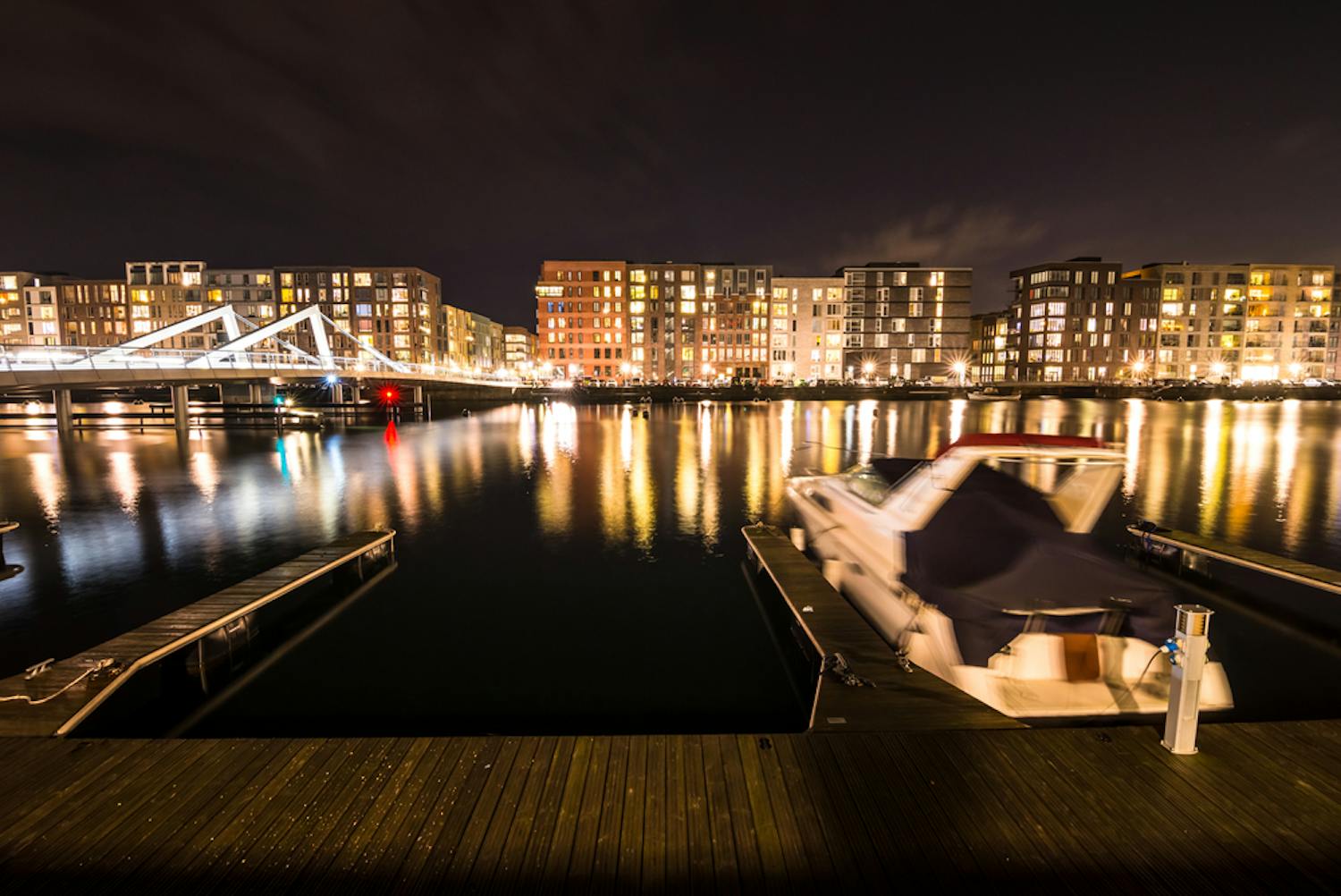 baad parkeret foran lysende bylandskab fotograferet med varm hvidbalance Båt ligger i docka framför lysande stadslandskap, bilden tagen med lång slutartid och varm vitbalans